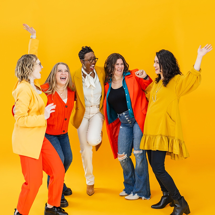 Five mothers of various ethnicities wearing bright colors, smiling and celebrating their joy because they love working for MomCo.